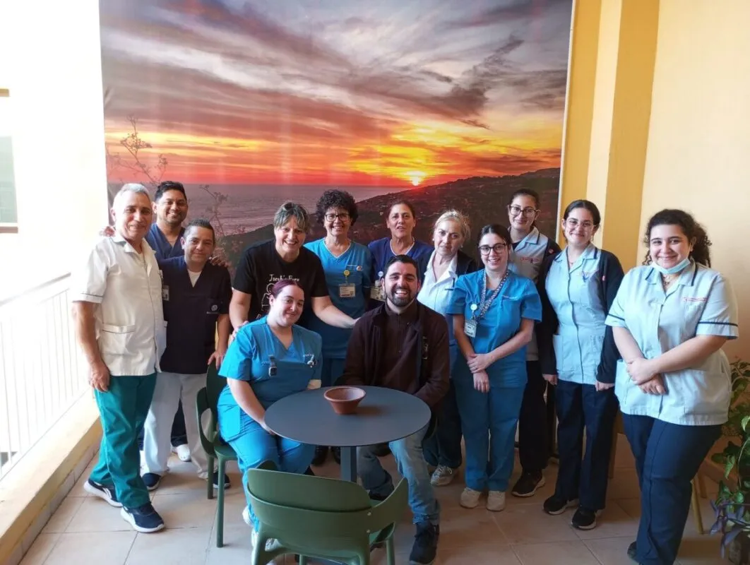 Hospital staff in scrubs gathered with Jacob on one of the refurbished terraces, in front of a large sunset mural