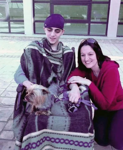 The photo that started it all: Jacob, wrapped in a blanket in a wheelchair outside Mater Dei Hospital in 2013, reunited with the family Yorkshire Terrier Peanut